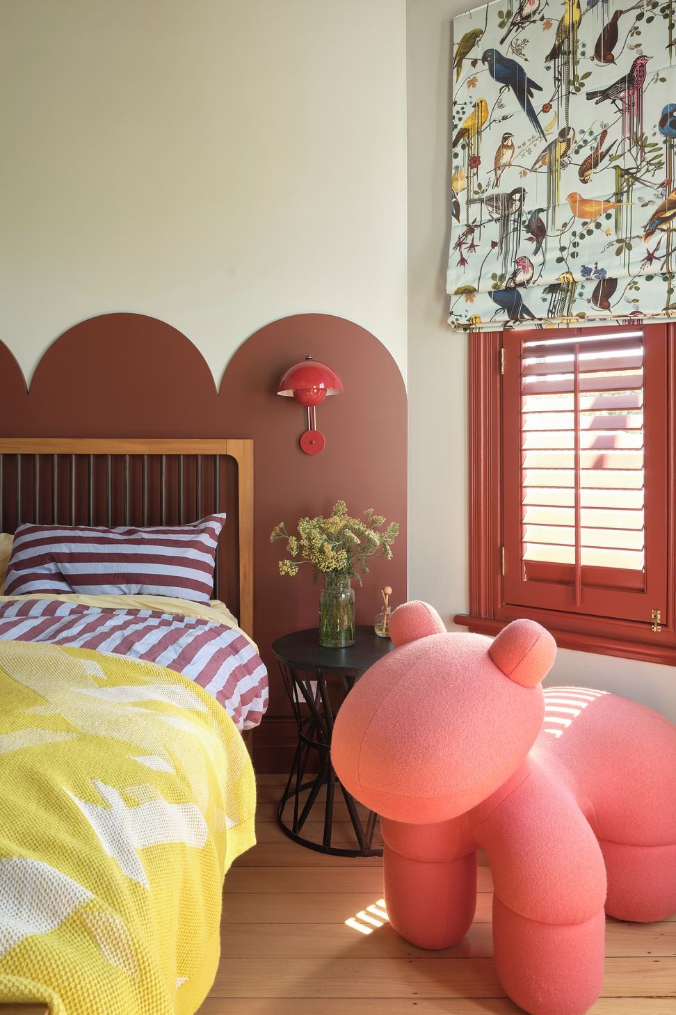 Turnbull bedroom with deep red window shutters, a scalloped bedhead and playful pink seating.
